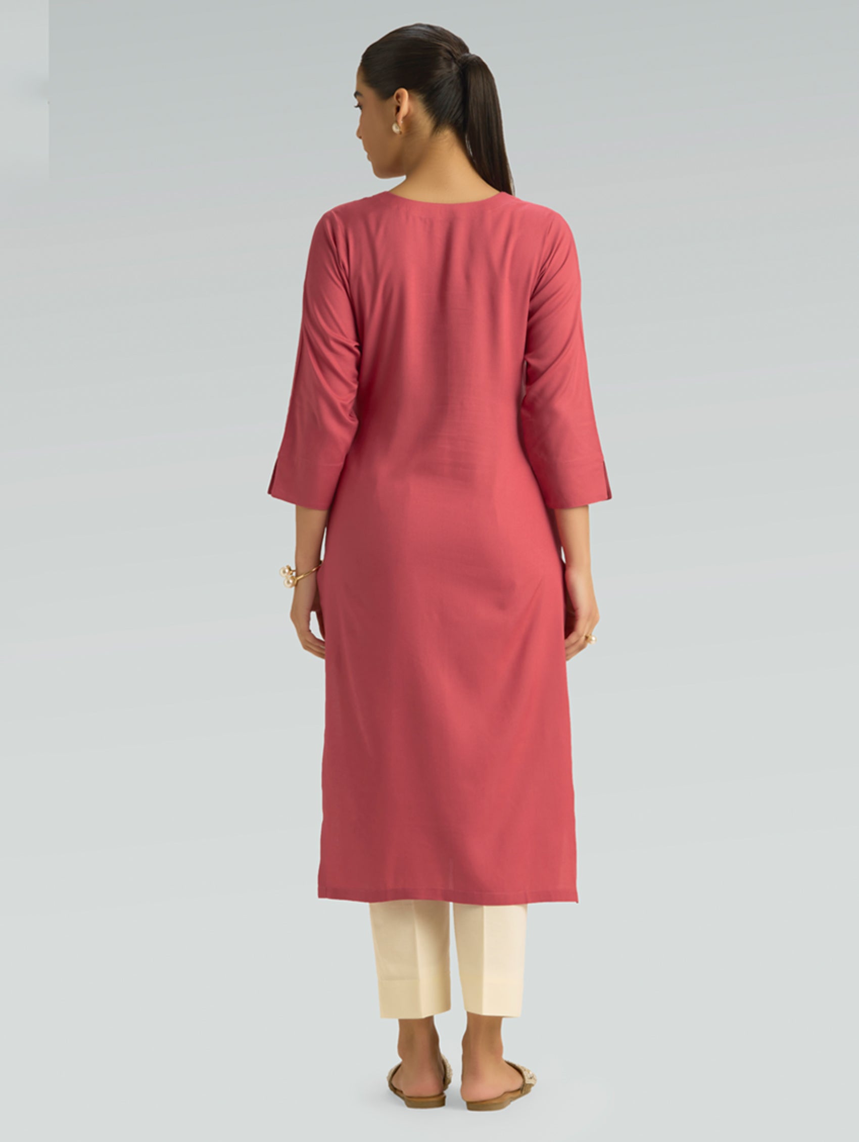 “A woman dressed in a pink kurta with beige pants, captured in a graceful back pose against a light gray background.”