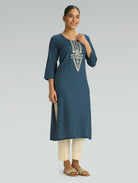 Woman wearing a blue embroidered kurta with white pants on a gray background