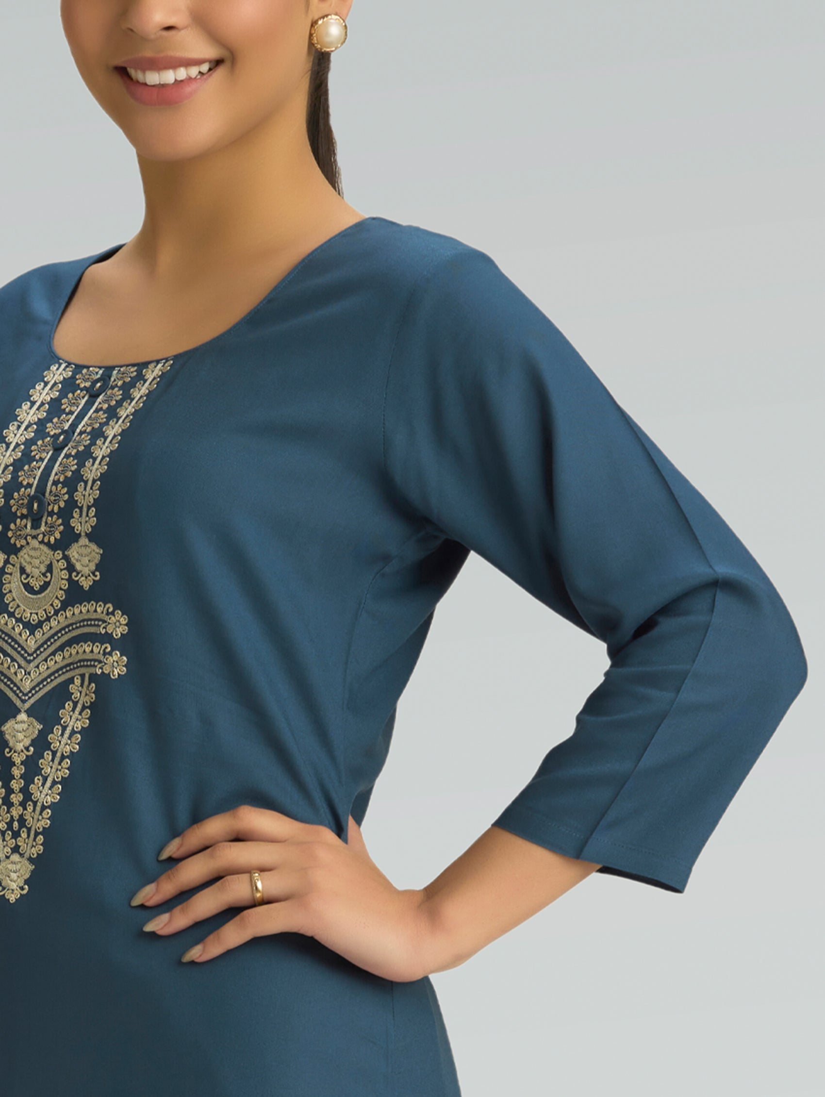 Woman wearing a blue dress with gold embroidery on a gray background