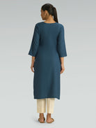 “A woman dressed in a teal kurta paired with beige pants, captured in a graceful back pose on a light gray background.”