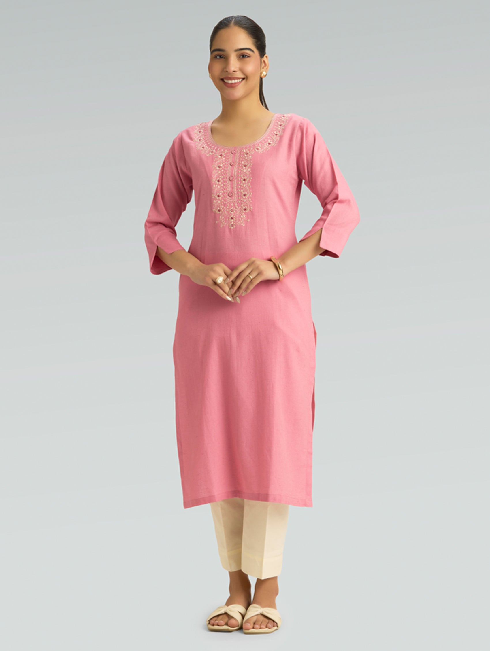 “A woman dressed in a straight-fit pink kurta featuring a round collar and intricate computerized thread embroidery, set against a gray background.”
