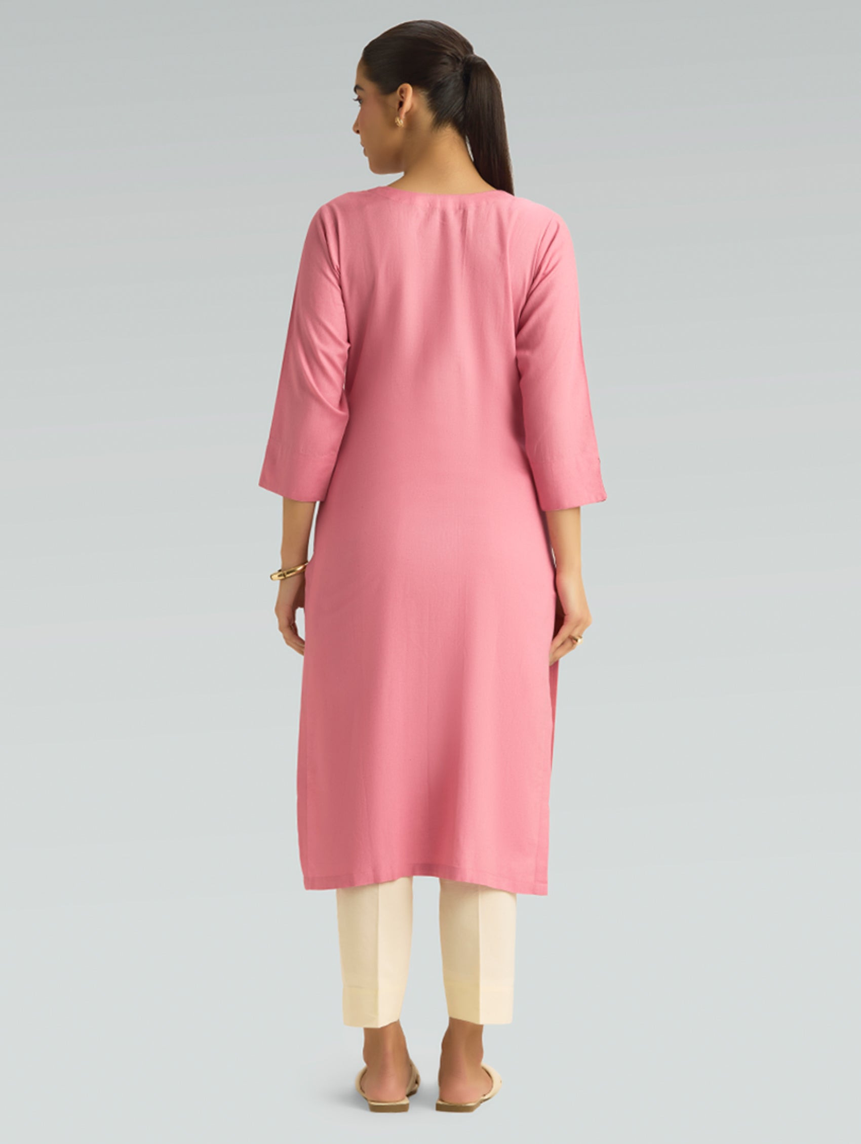 “A woman dressed in a pink kurta paired with white pants, captured in a graceful back pose on a light gray background.”