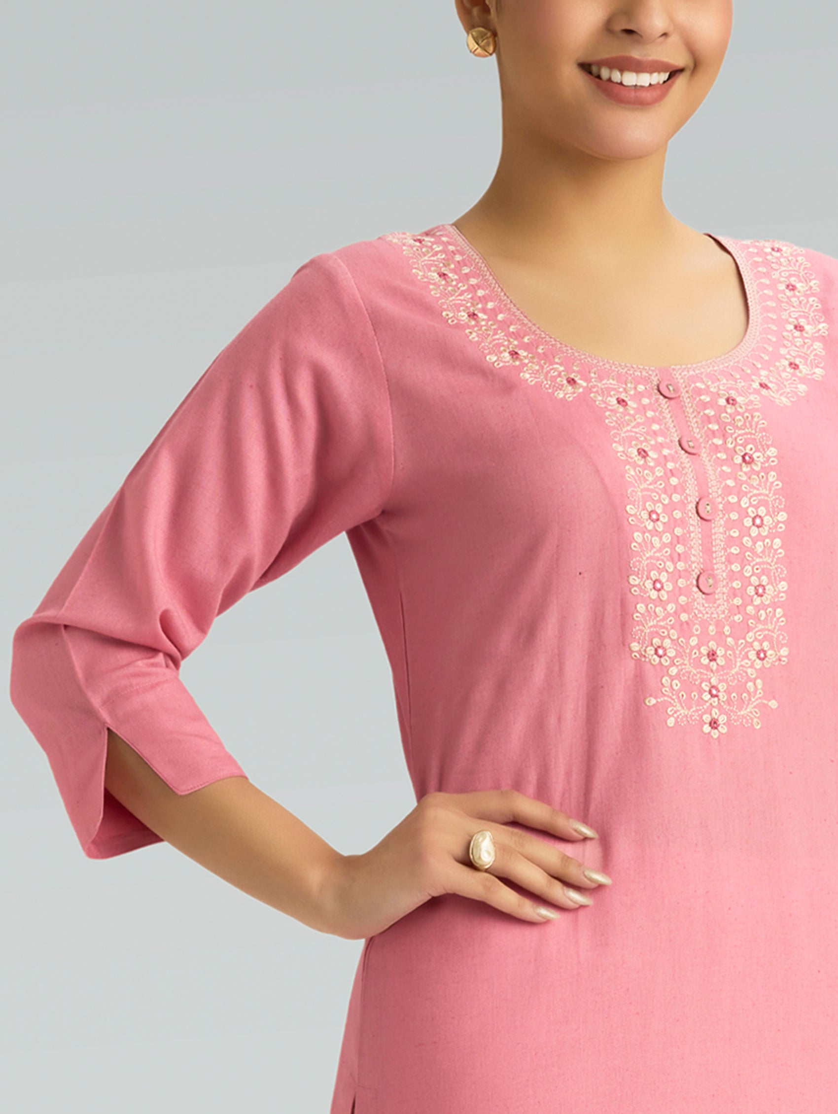 Woman wearing a pink dress with intricate white embroidery on a gray background