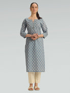“A woman wearing a straight-fit gray patterned kurta with a round neckline, paired with beige pants, on a light gray background.”