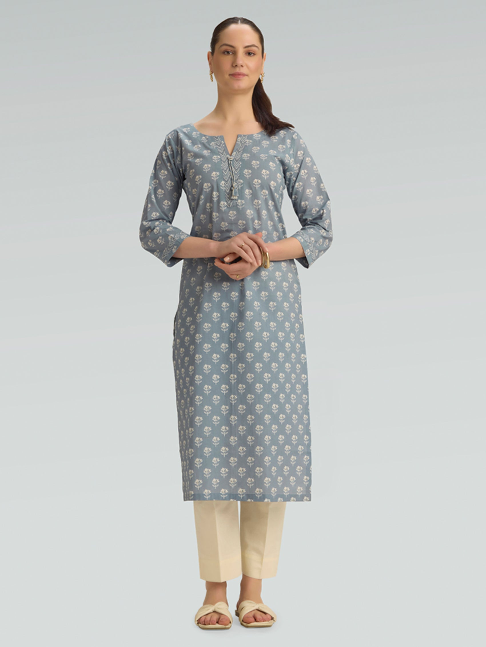 “A woman wearing a straight-fit gray patterned kurta with a round neckline, paired with beige pants, on a light gray background.”