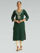 “A woman wearing a straight-fit green kurta with a round neckline and computerized thread embroidery, set against a gray background.”