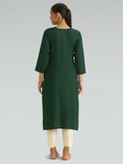 “A woman dressed in a green kurta paired with white pants, captured in a graceful back pose on a light gray background.”