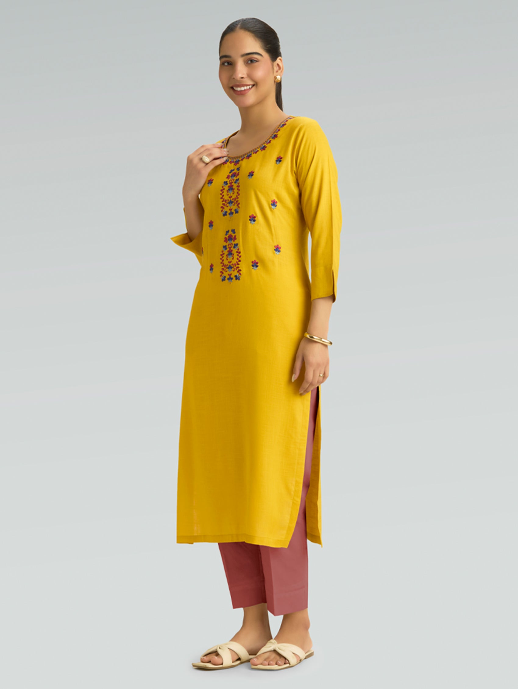 Woman wearing a yellow kurta with pink pants on a gray background