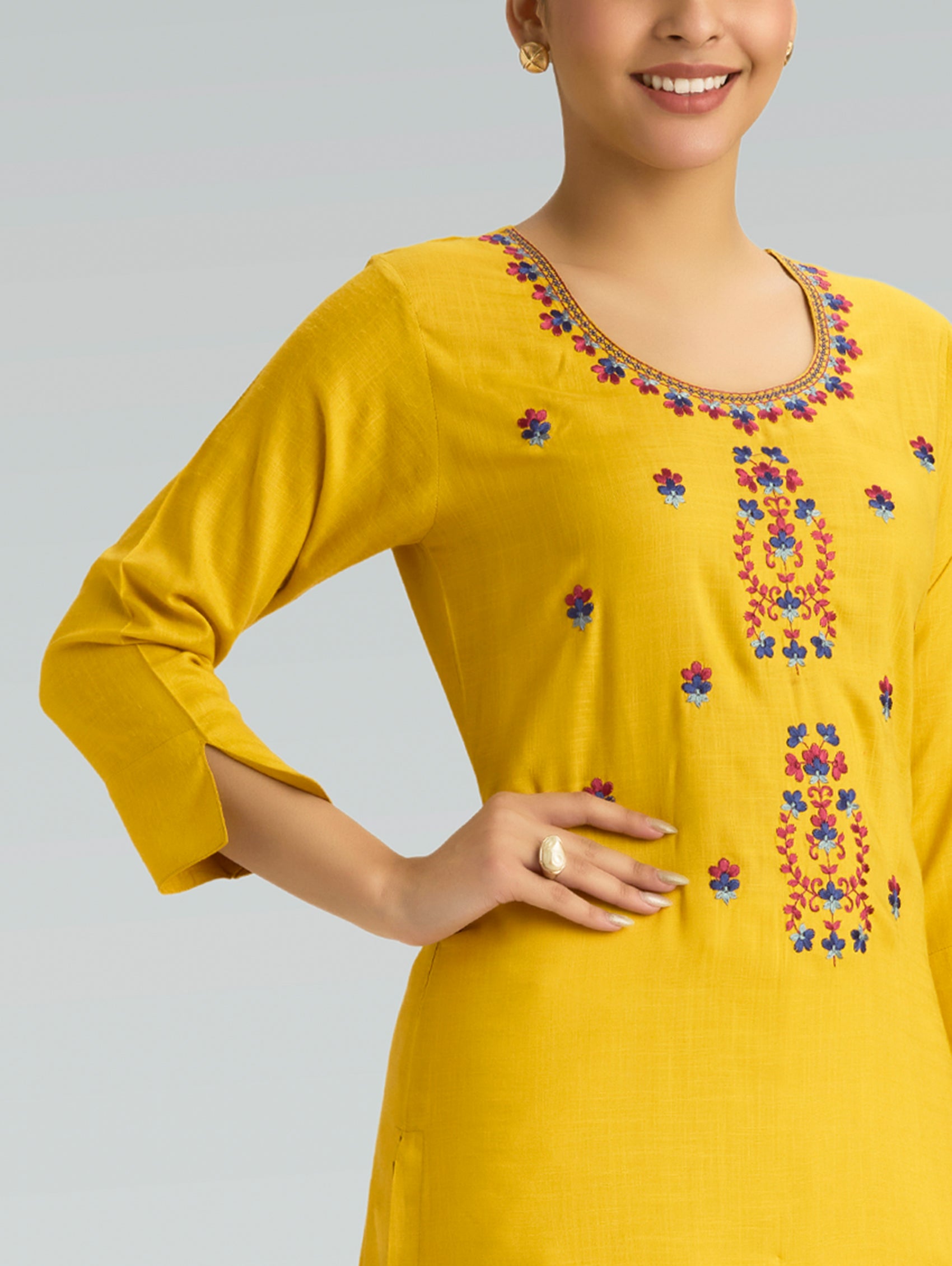 Woman wearing a yellow kurta with floral embroidery on a light gray background