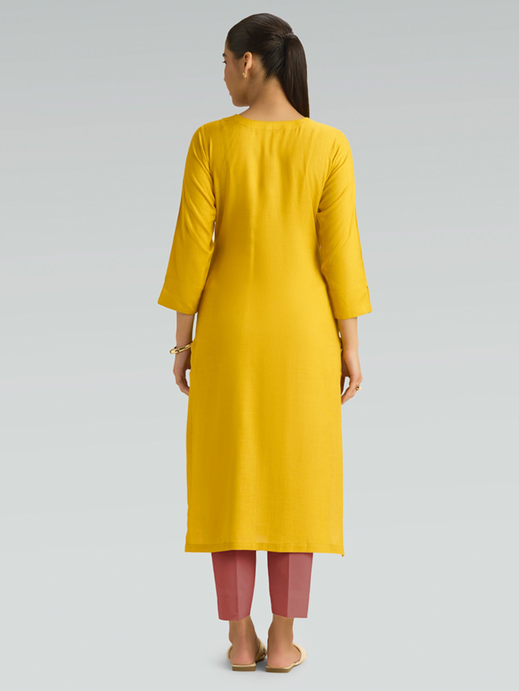 “A woman wearing a yellow kurta, shown from the back against a plain background.”