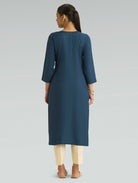 “A woman wearing a blue kurta with beige pants, shown from the back against a gray background.”