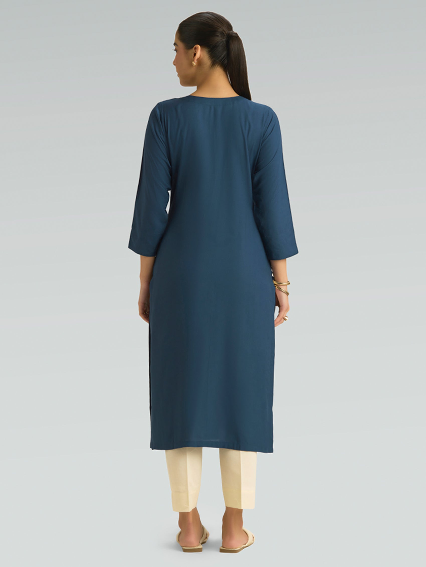 “A woman wearing a blue kurta with beige pants, shown from the back against a gray background.”