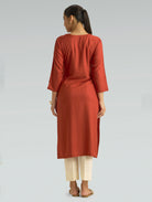 A woman in a red kurta paired with white pants, shown in a back pose against a light gray background.