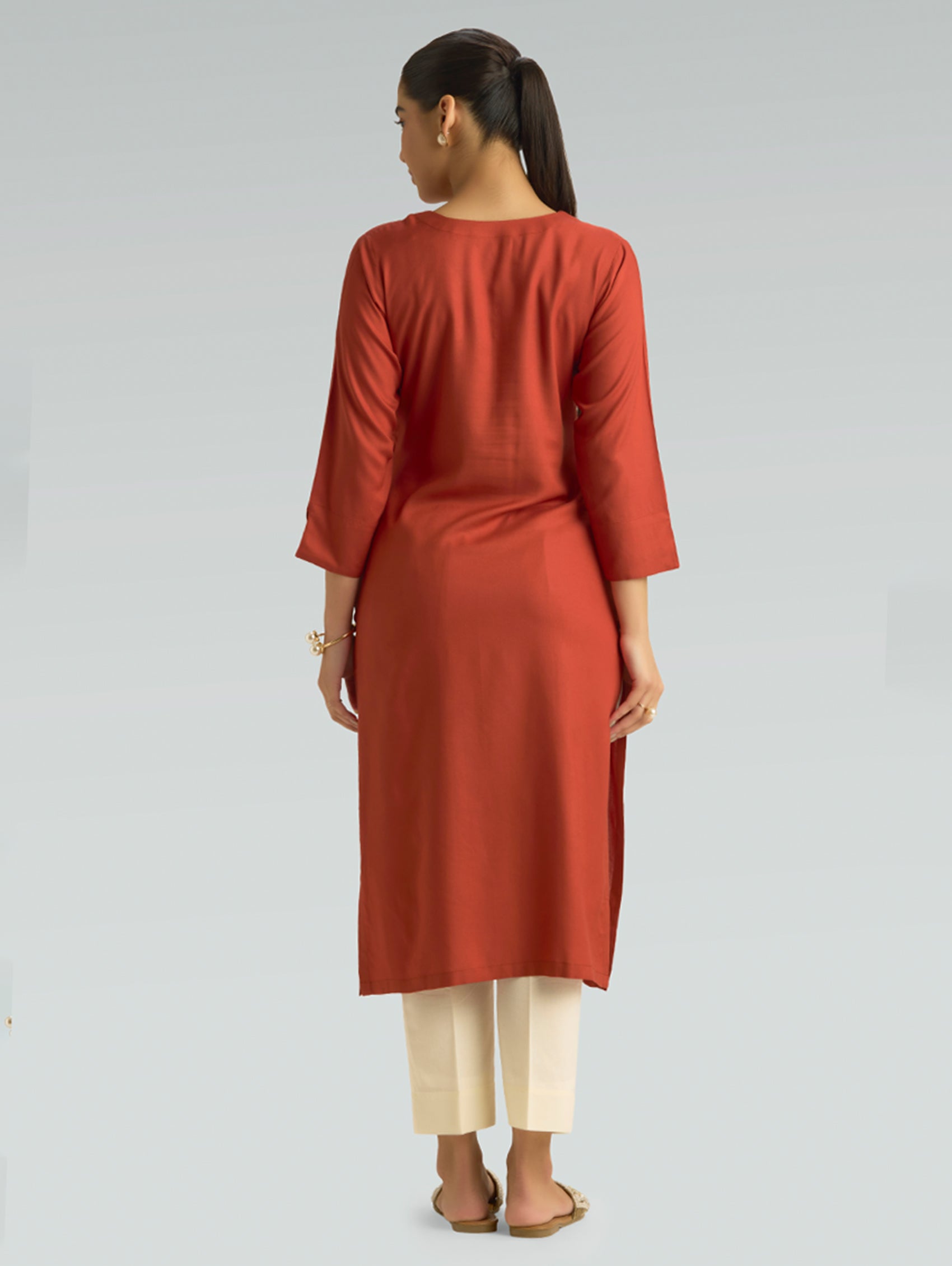 A woman in a red kurta paired with white pants, shown in a back pose against a light gray background.