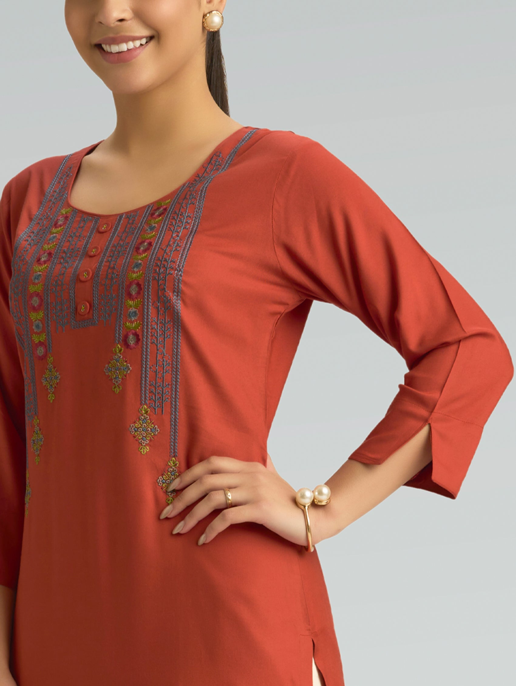 Woman wearing a rust-colored kurta with intricate embroidery on a plain background