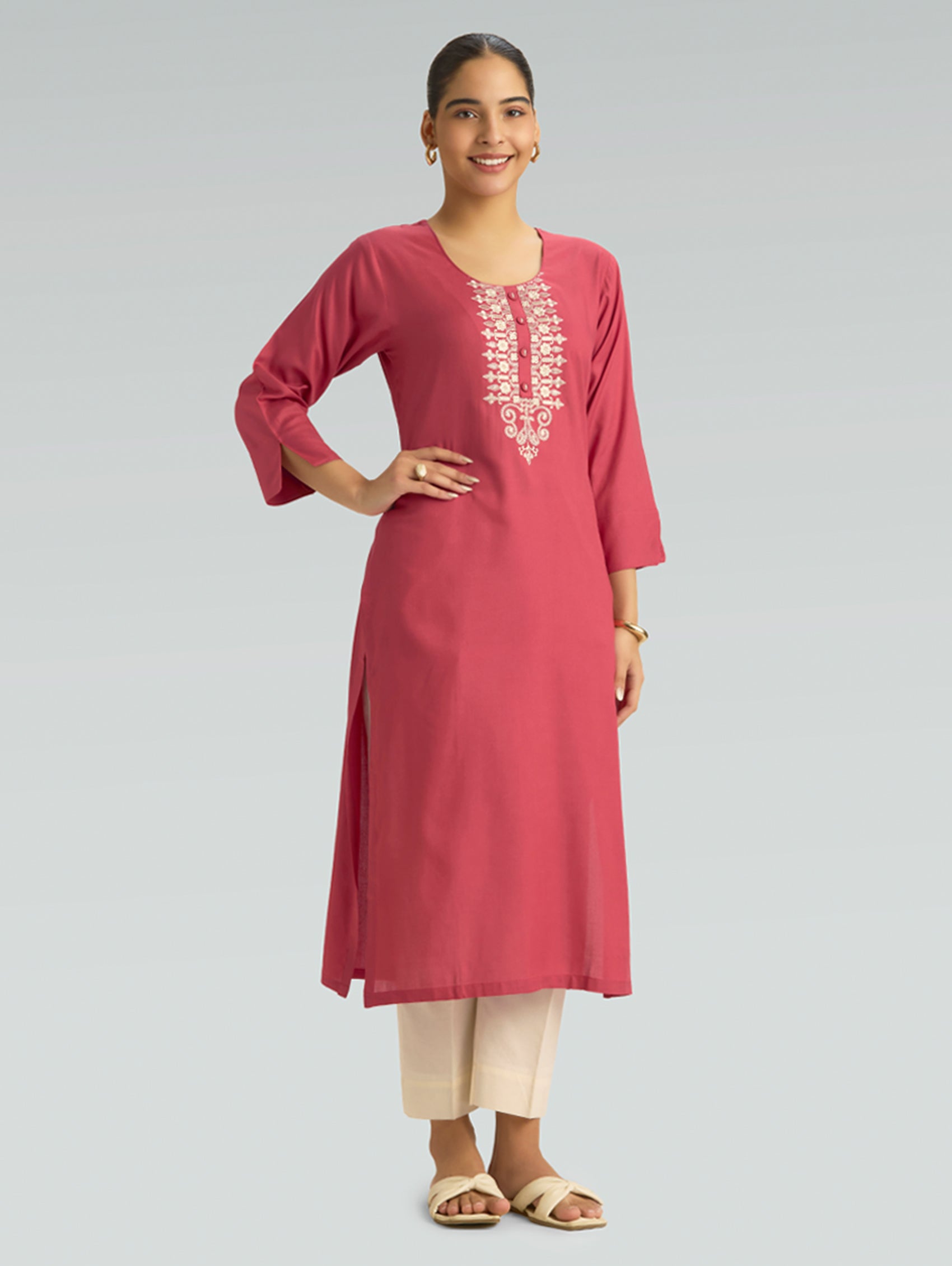 A woman wearing a straight-fit pink kurta with a round neckline, adorned with computerized thread embroidery, set against a soft gray background.