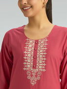 A woman wearing a straight-fit pink kurta with a round neckline, adorned with computerized thread embroidery, set against a soft gray background.