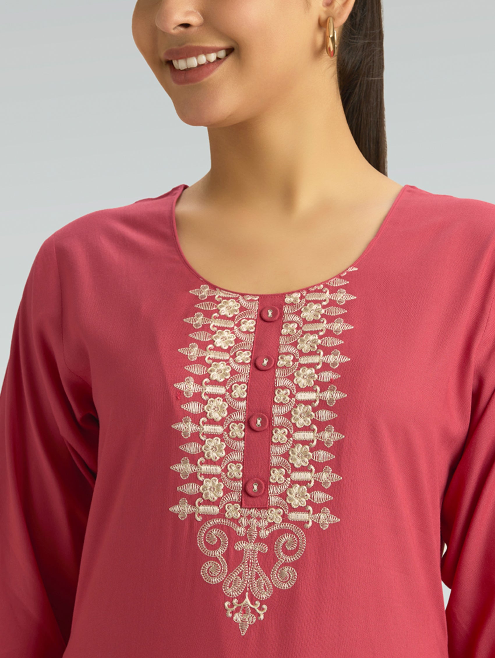 A woman wearing a straight-fit pink kurta with a round neckline, adorned with computerized thread embroidery, set against a soft gray background.