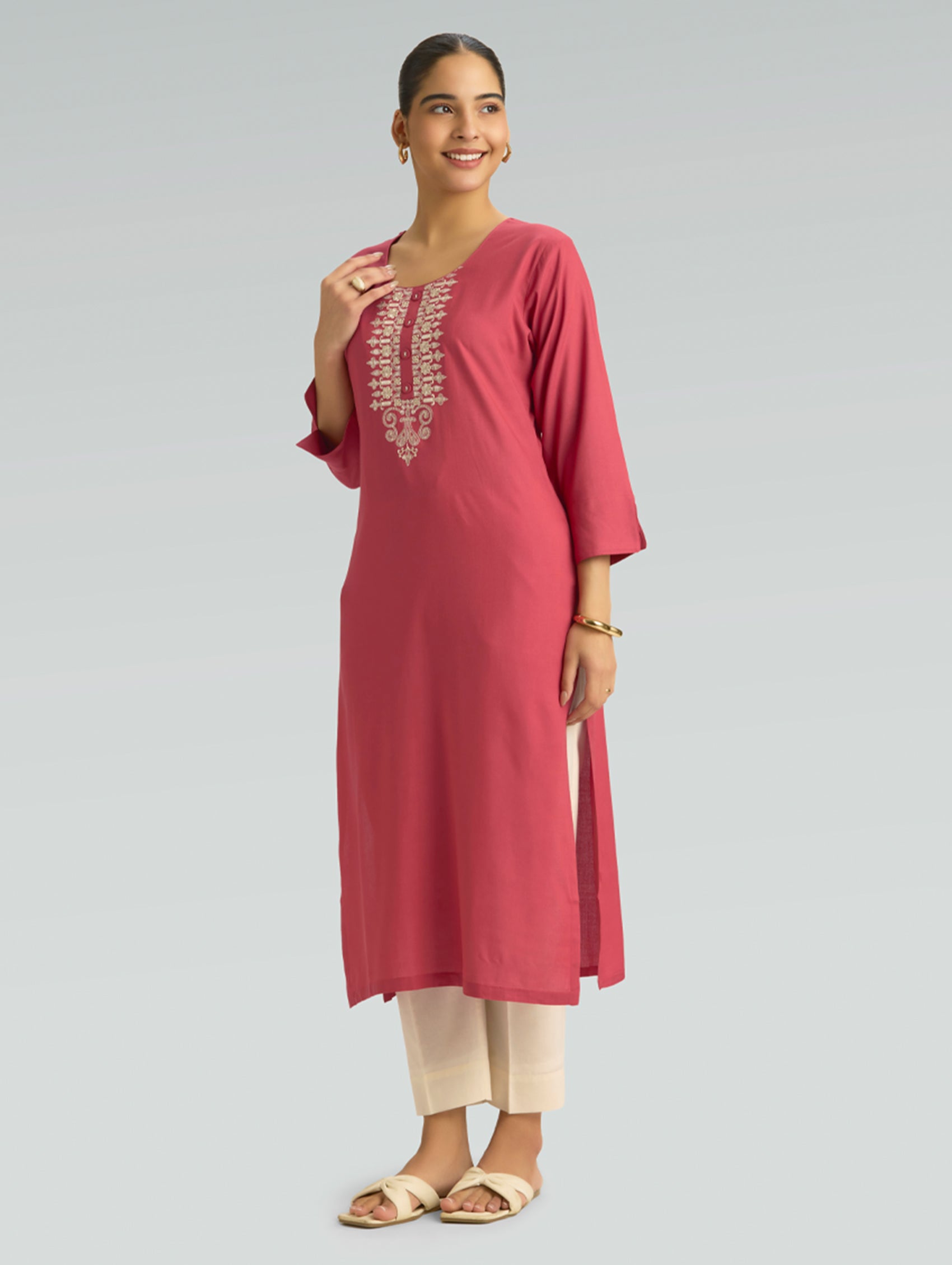 A woman wearing a straight-fit pink kurta with a round neckline, adorned with computerized thread embroidery, set against a soft gray background.