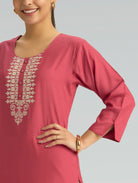 A woman wearing a straight-fit pink kurta with a round neckline, adorned with computerized thread embroidery, set against a soft gray background.