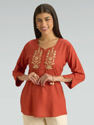 Woman wearing a red kurta with gold embroidery on a gray background
