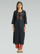 A woman wearing a straight-fit black kurta with a round neckline, adorned with floral embroidery, set against a soft gray background.