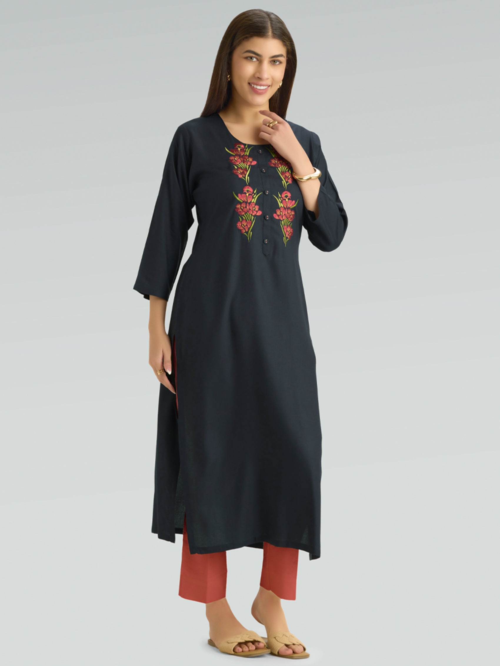 Woman wearing a black kurta with red floral embroidery on a gray background