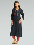 Woman wearing a black embroidered kurta with red pants on a gray background