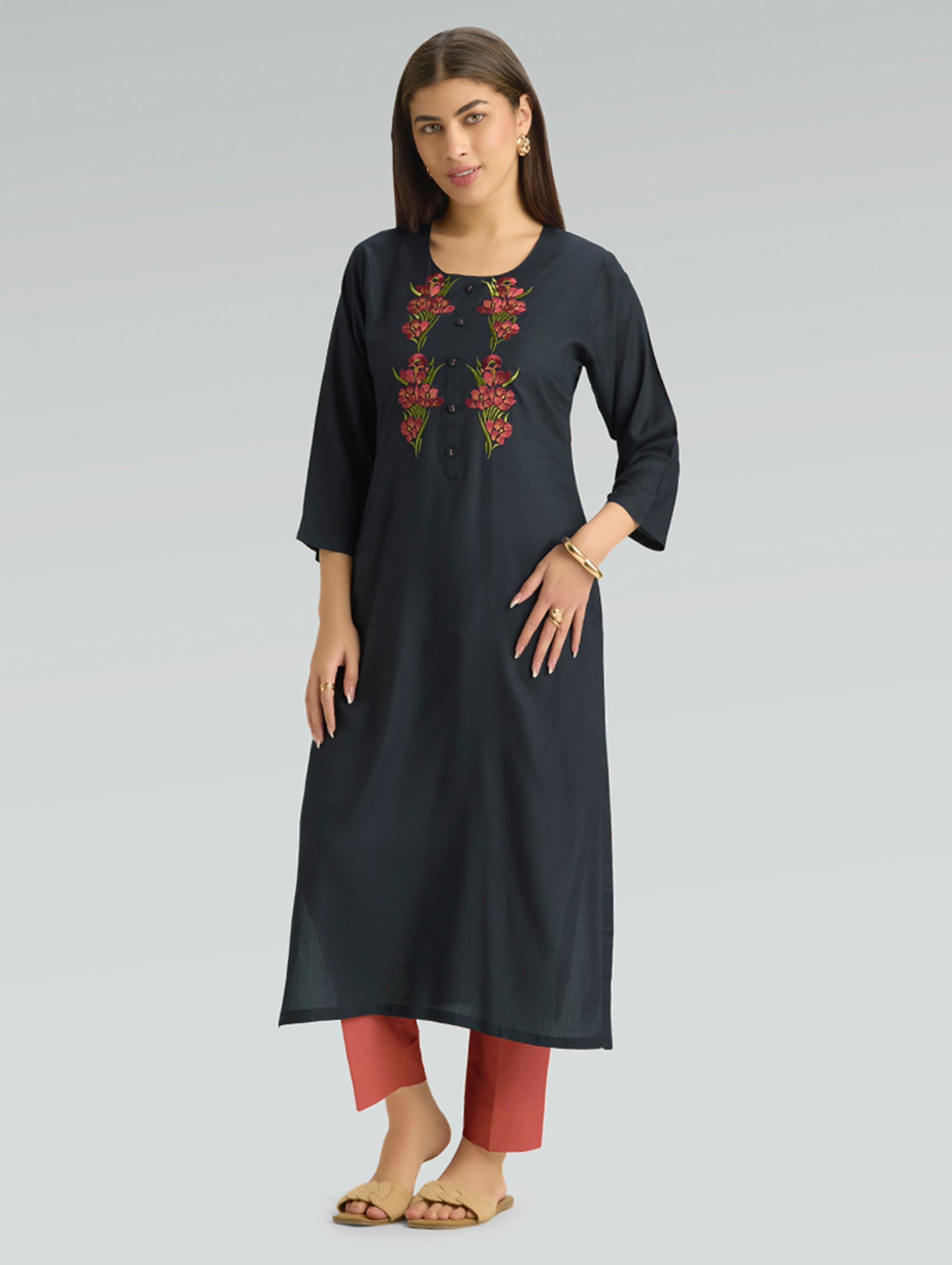 Woman wearing a black embroidered kurta with red pants on a gray background