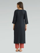 A woman in a straight-fit black kurta with a round neckline and floral embroidery, shown in a back pose against a soft gray background.