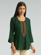 Woman wearing a green embroidered top against a gray background