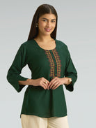 Woman wearing a green top with embroidery on a gray background