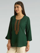 Woman wearing a green top with embroidery on a gray background