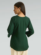 Woman wearing a green long-sleeve top against a gray background