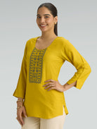 Woman wearing a yellow top with embroidery on a gray background
