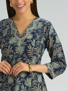 Woman wearing a navy blue floral patterned dress with gold jewelry on a gray background