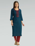 A woman wearing a straight-fit teal kurta with a round neckline, adorned with intricate red embroidery, set against a soft gray background.