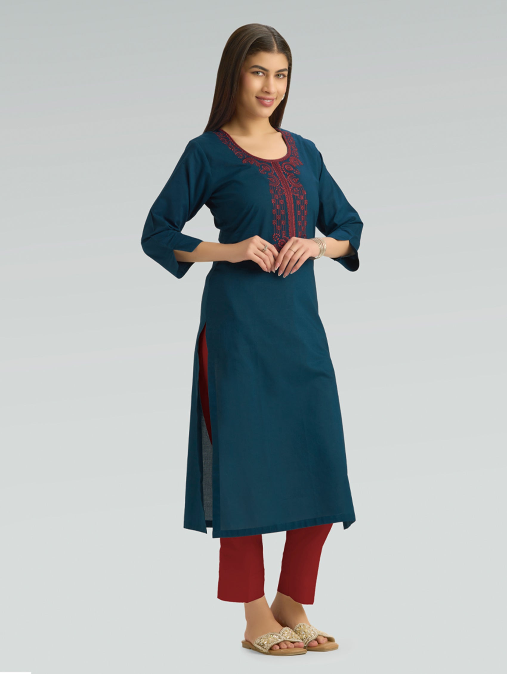Woman wearing a teal kurta with red embroidery on a gray background