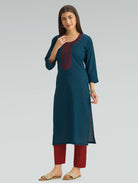 Woman wearing a teal kurta with red embroidery and red pants on a light gray background