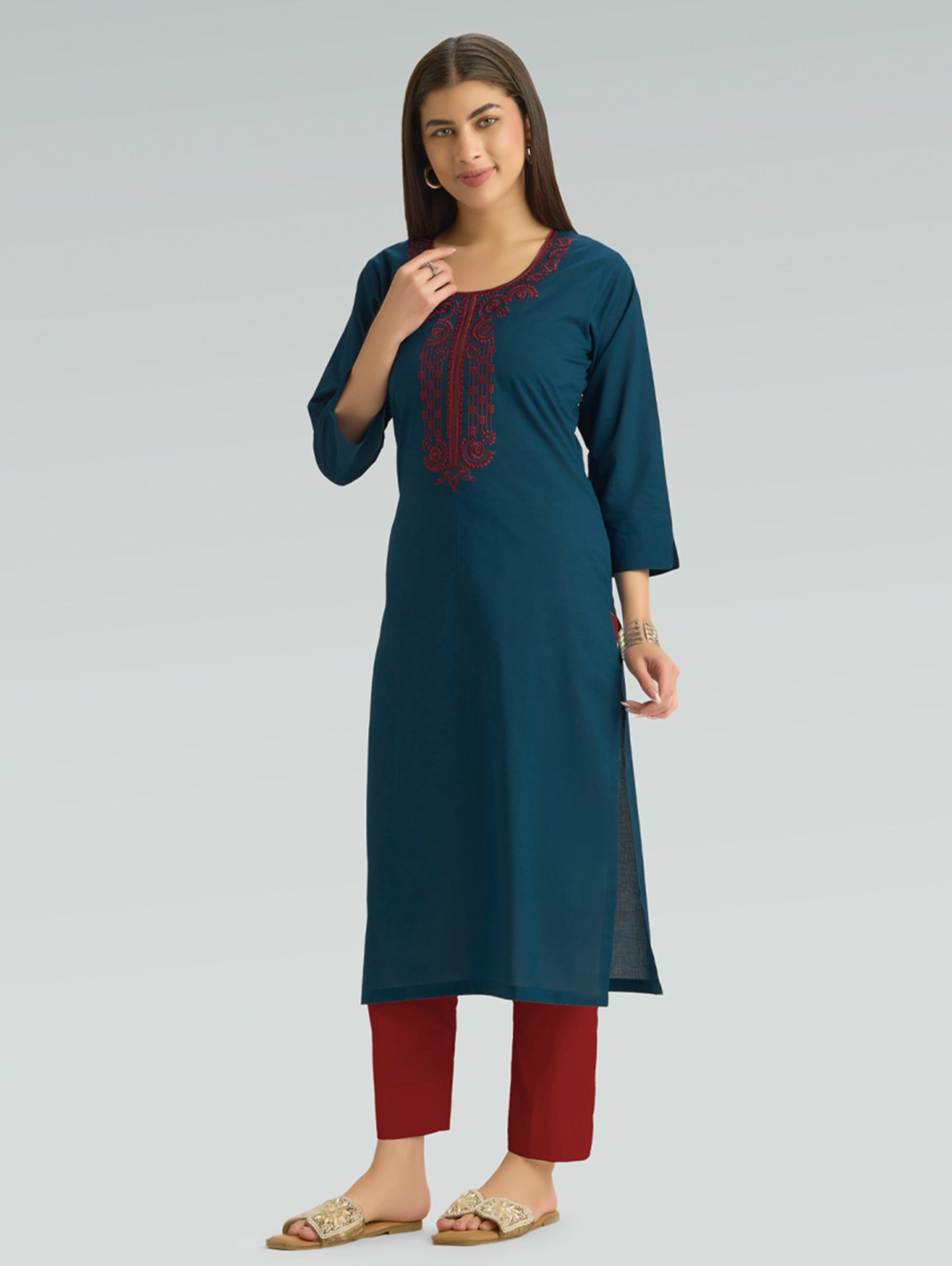 Woman wearing a teal kurta with red embroidery and red pants on a light gray background