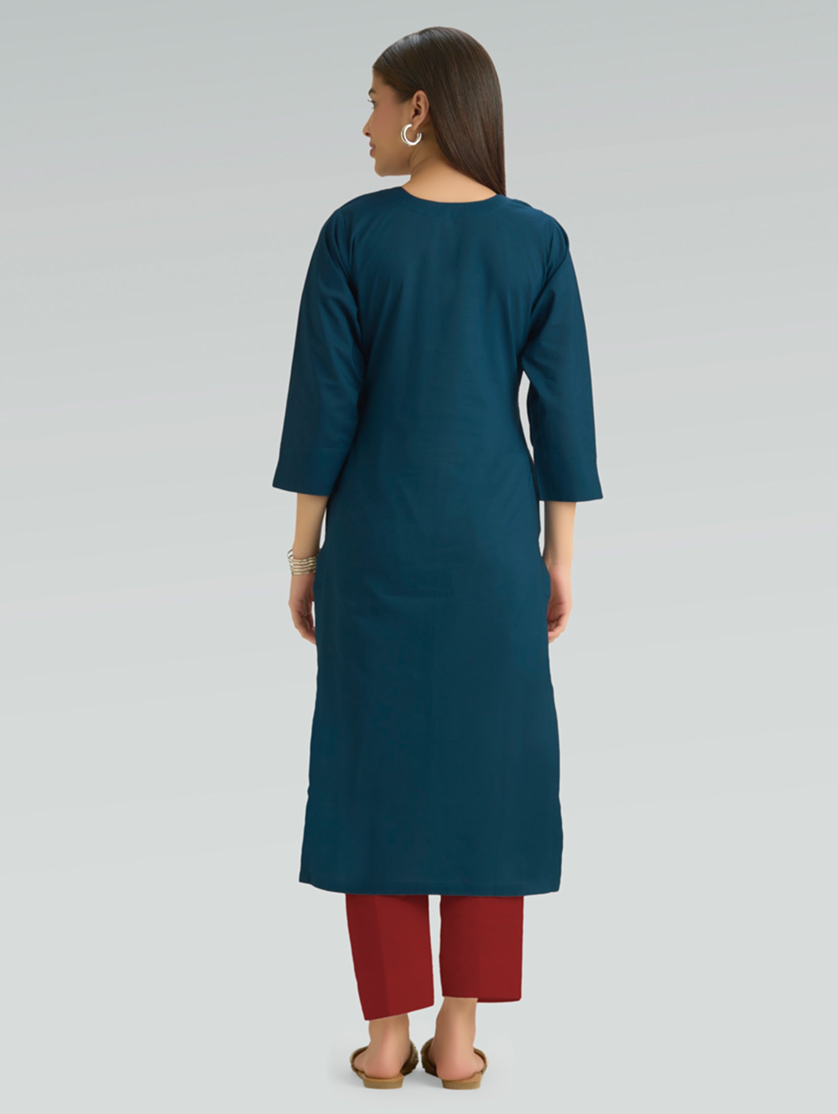 A woman in a teal kurta paired with red pants, shown in a back pose against a gray background.