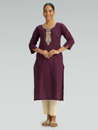 A woman dressed in a straight-fit purple kurta with a round neckline, beautifully adorned with computerized thread embroidery, styled with beige pants against a soft gray background.