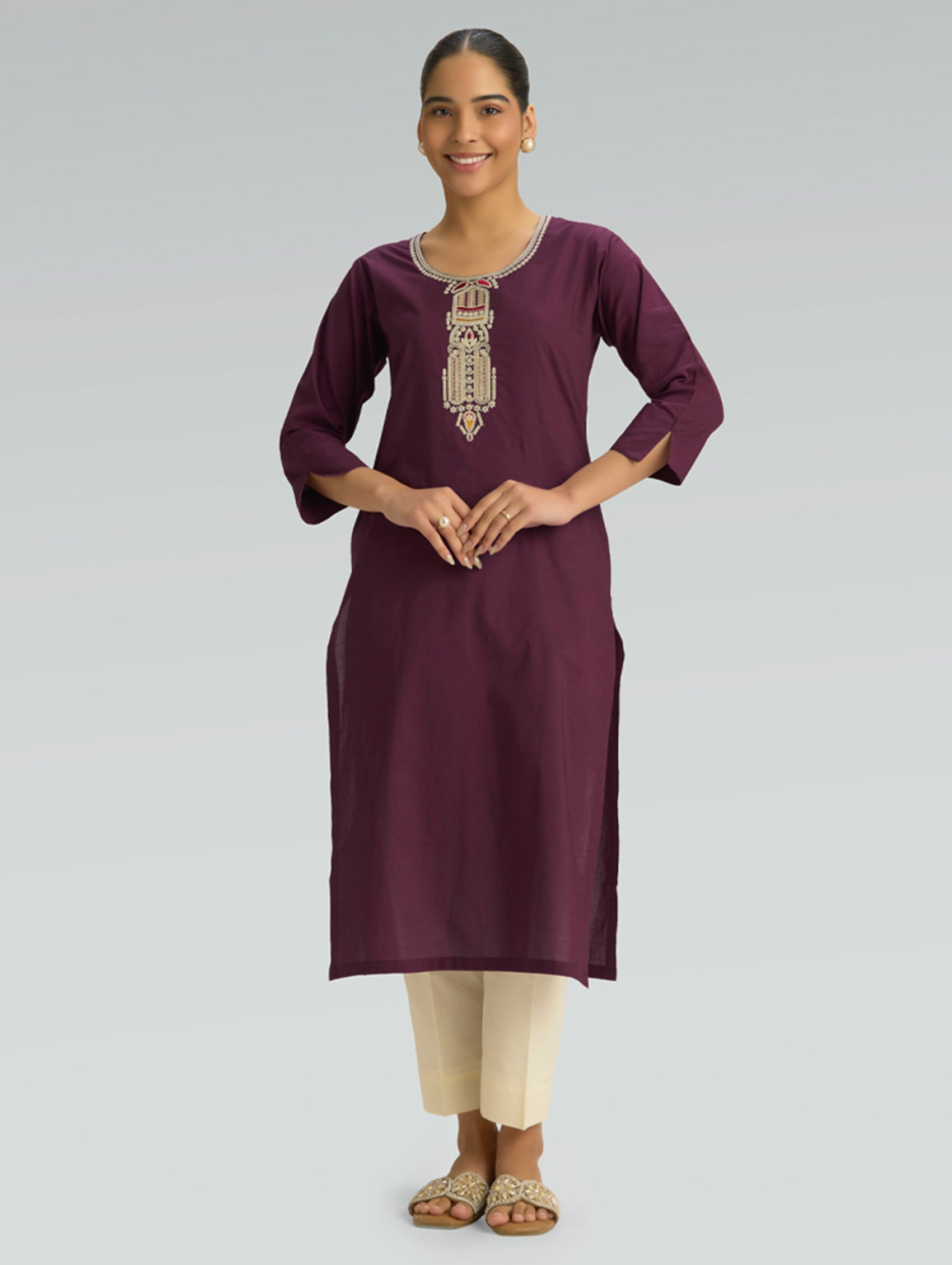 A woman dressed in a straight-fit purple kurta with a round neckline, beautifully adorned with computerized thread embroidery, styled with beige pants against a soft gray background.