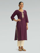 Woman wearing a maroon kurta with white embroidery on a gray background