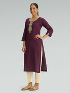 Woman wearing a purple kurta with white pants on a gray background