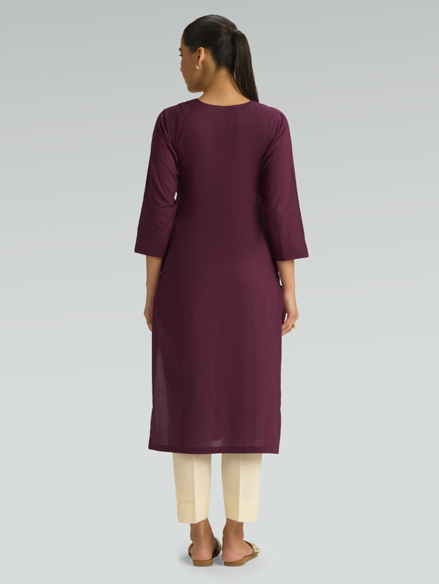 A woman in a purple kurta paired with beige pants, shown in a back pose against a light gray background.