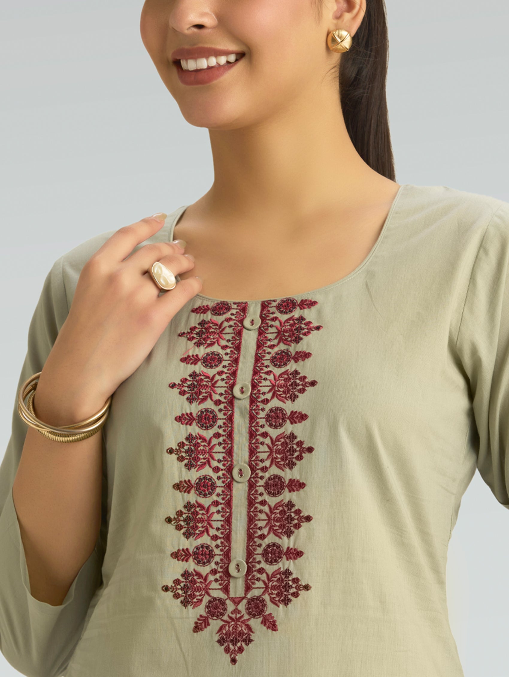 Woman wearing a light green kurta with red embroidery on a plain background