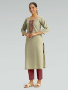 Woman wearing a light green kurta with maroon embroidery and red pants on a gray background