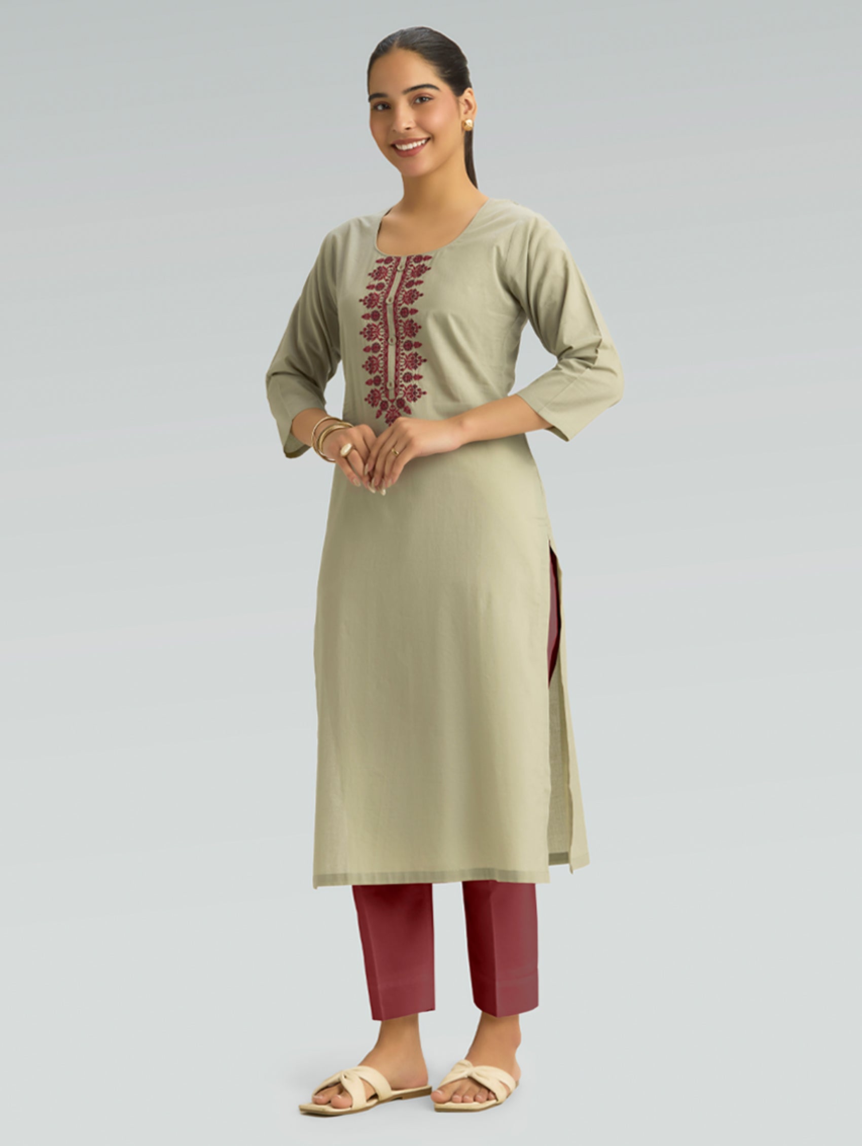 Woman wearing a light green kurta with maroon embroidery and red pants on a gray background