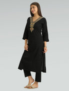 Woman wearing a black kurta with gold embroidery on a gray background